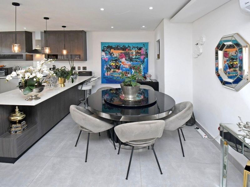 Modern open-plan kitchen and dining area featuring a sleek kitchen island, contemporary cabinetry, recessed lighting, and neutral tiled flooring.