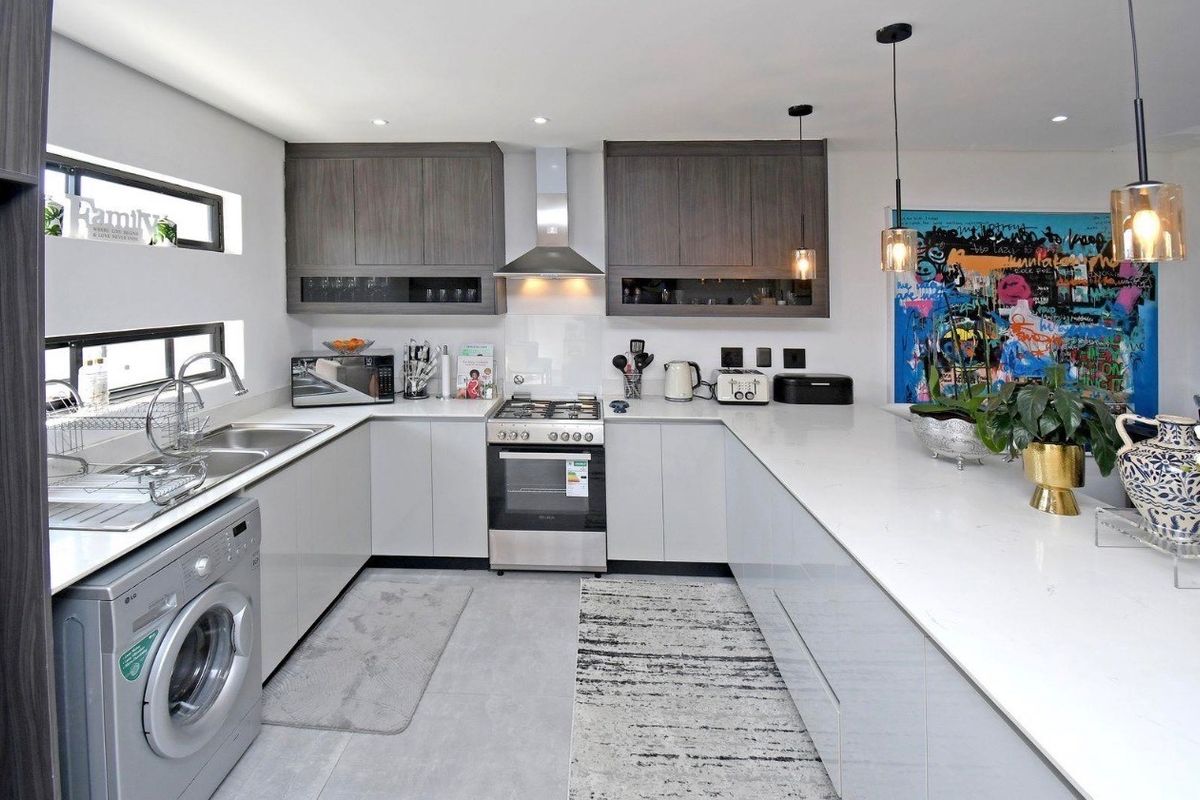 Modern kitchen featuring sleek grey cabinetry, stone countertops, stainless steel gas stove, extractor fan, and integrated laundry facilities with recessed and pendant lighting.