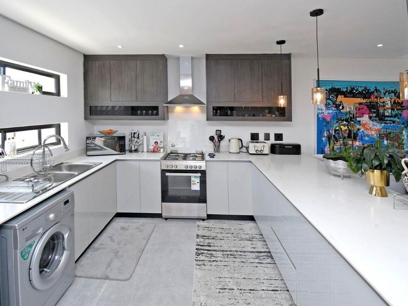 Modern kitchen featuring sleek grey cabinetry, stone countertops, stainless steel gas stove, extractor fan, and integrated laundry facilities with recessed and pendant lighting.