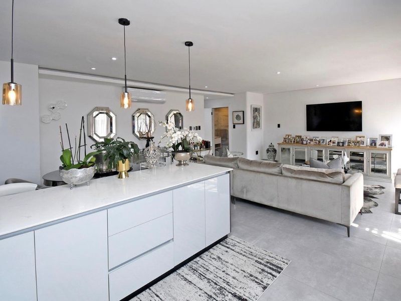 Modern open-plan living area featuring a sleek kitchen island with stone countertops, recessed lighting, and neutral tiled flooring throughout.
