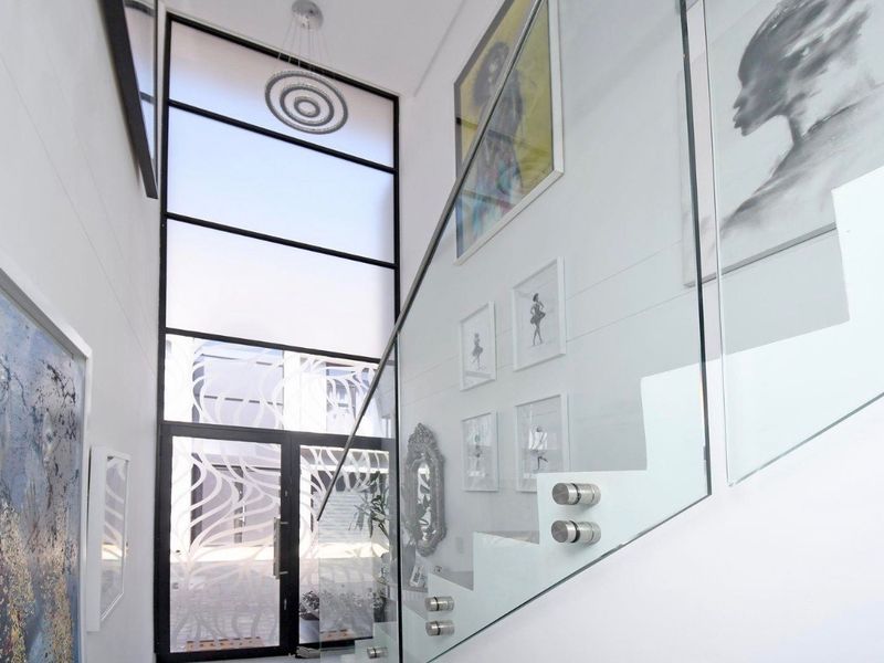 A bright and modern double-volume entrance hall featuring a sleek glass staircase balustrade and a large feature window.