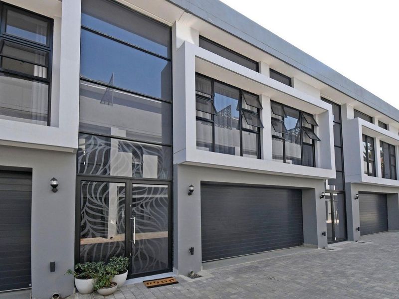 Modern double-storey townhouse facade featuring contemporary grey and white finishes, large glass windows, and integrated garage access.