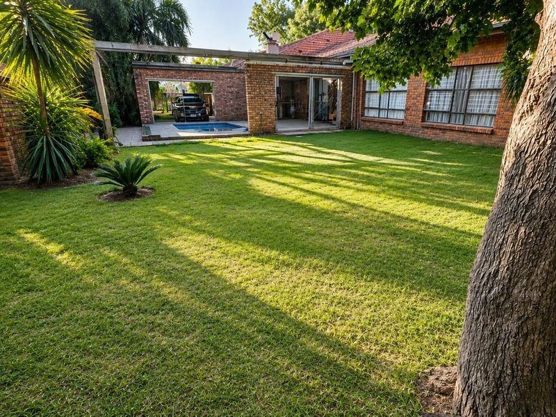 A spacious rear garden featuring a well-maintained lawn, brick exterior facade, and a swimming pool area with sliding door access to the home.