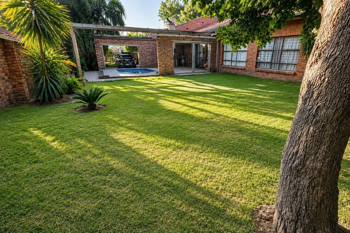 A spacious rear garden featuring a well-maintained lawn, brick exterior facade, and a swimming pool area with sliding door access to the home.