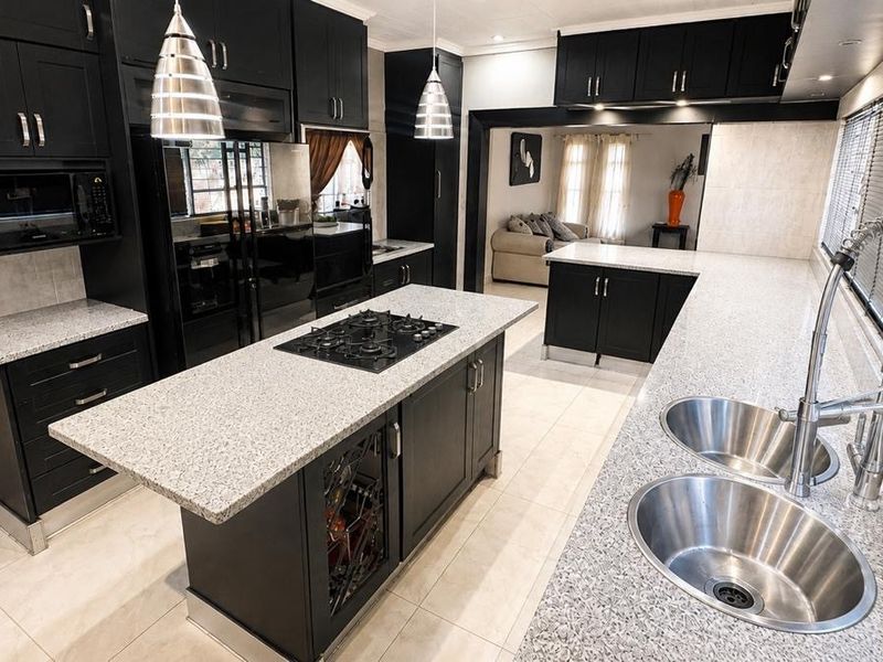 Modern kitchen featuring black cabinetry, granite countertops, a central island with a gas hob, and double basin sink with a gooseneck faucet.