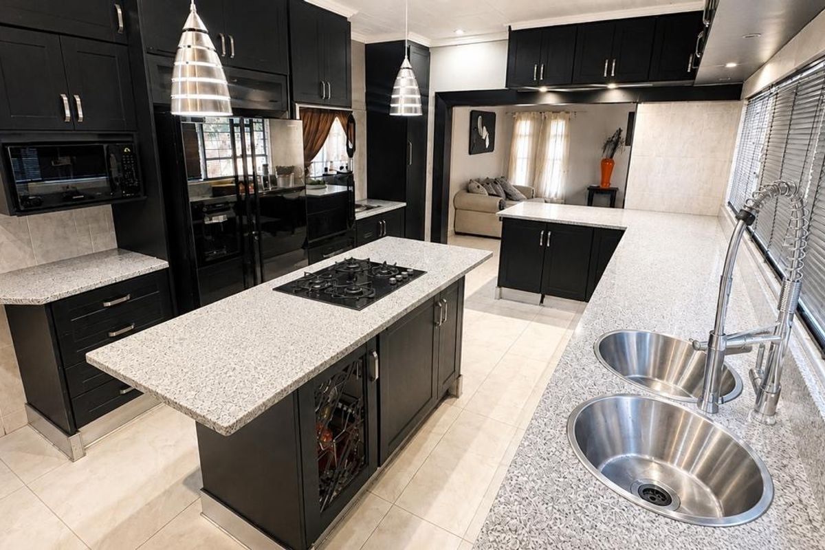 Modern kitchen featuring black cabinetry, granite countertops, a central island with a gas hob, and double basin sink with a gooseneck faucet.