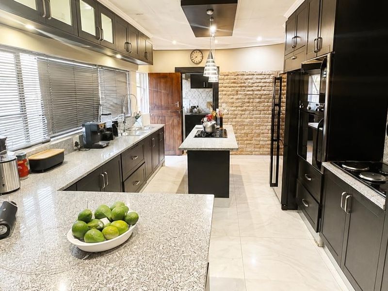 Modern kitchen featuring dark cabinetry, granite countertops, a central island with a hob, and an exposed brick feature wall.