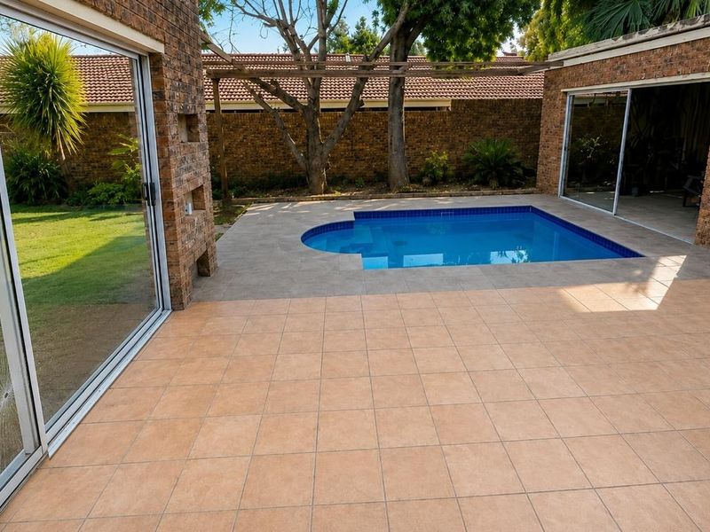 Outdoor entertainment area featuring a swimming pool, tiled patio, and brick exterior walls, with direct access through sliding glass doors.