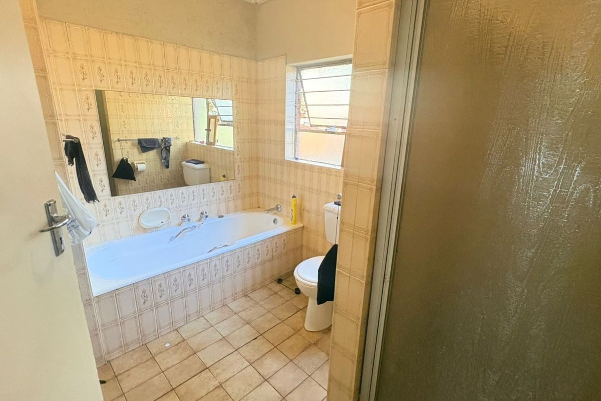 A dated bathroom featuring a built-in bathtub, ceramic tiling, and a toilet, offering potential for a modern renovation.