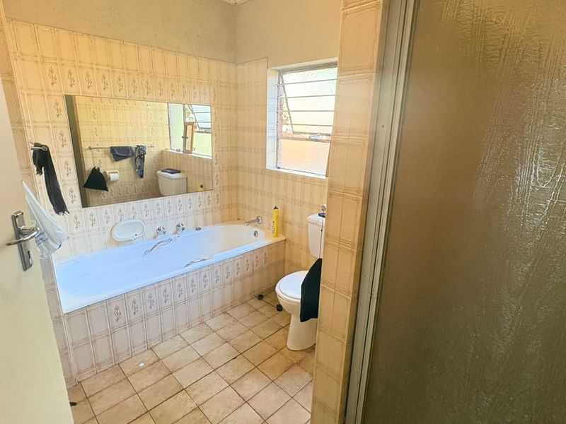 A dated bathroom featuring a built-in bathtub, ceramic tiling, and a toilet, offering potential for a modern renovation.