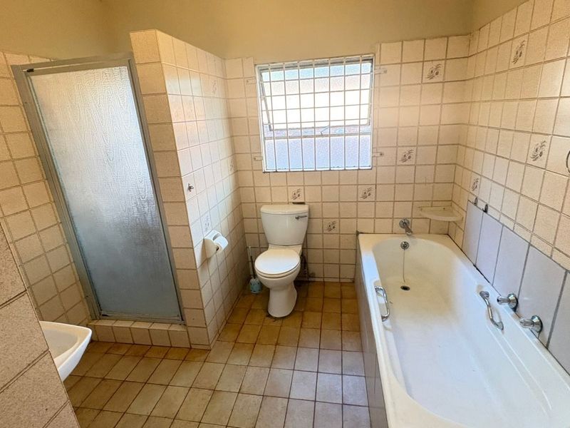 A dated bathroom featuring a bathtub, separate shower enclosure, and toilet, with original wall and floor tiling throughout.