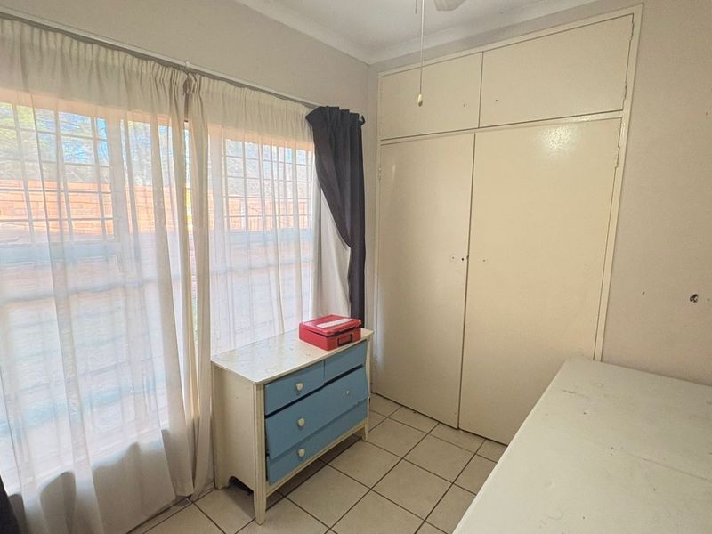 A bedroom featuring tiled flooring, built-in cupboards, and a large window allowing natural light.