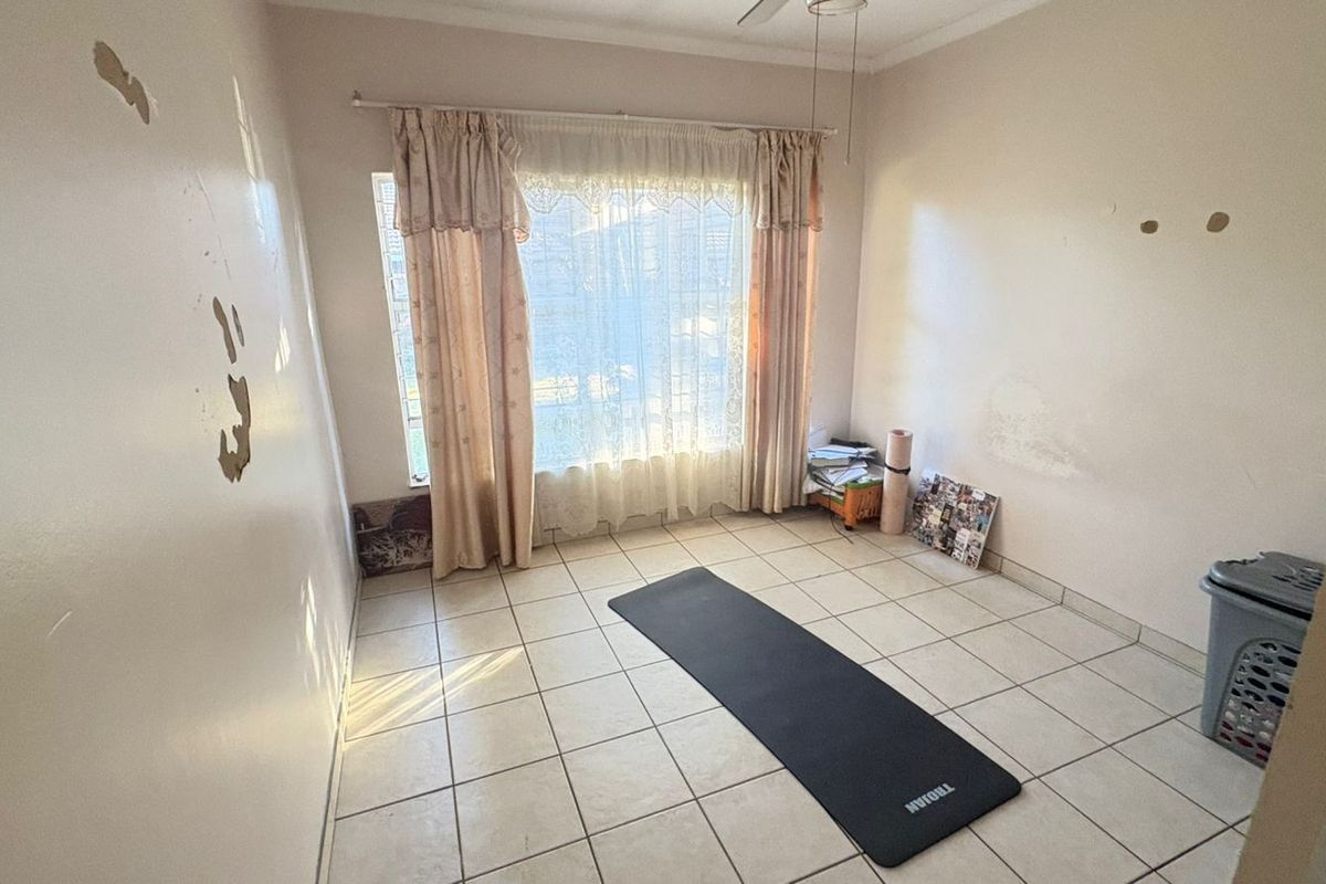 A vacant bedroom featuring tiled flooring, a ceiling fan, and window security bars, currently requiring wall repairs and repainting.