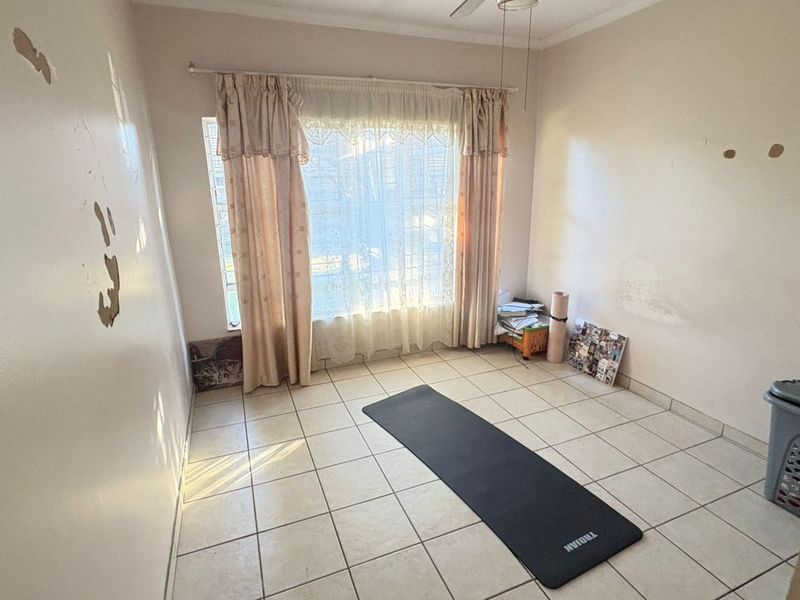 A vacant bedroom featuring tiled flooring, a ceiling fan, and window security bars, currently requiring wall repairs and repainting.