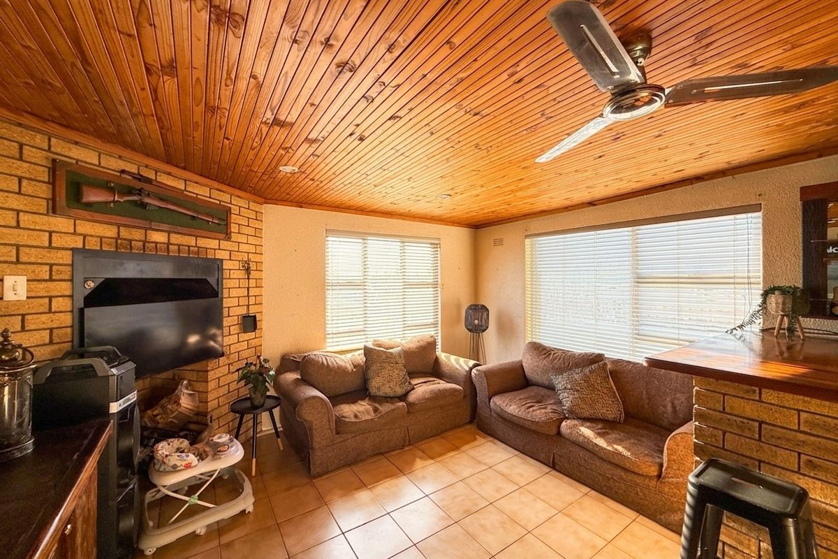 A cozy living room featuring a warm timber-clad ceiling, brick fireplace, and tiled flooring, offering a rustic and inviting atmosphere.