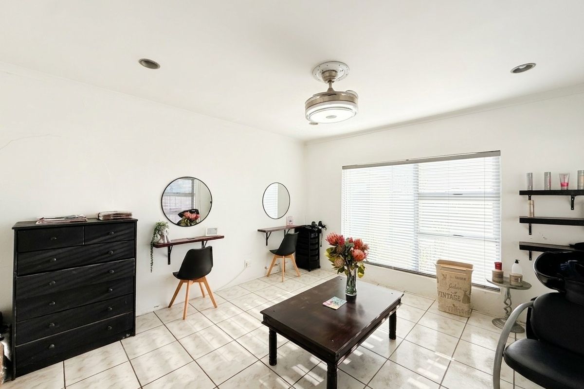 A versatile room featuring tiled flooring, recessed lighting, and a ceiling fan, currently utilized as a salon space with natural light from large windows.