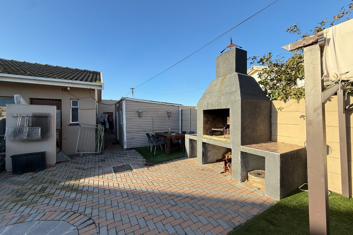 Rear outdoor entertainment area featuring a large built-in braai, paved patio, and artificial lawn, providing a functional space for outdoor dining and relaxation.