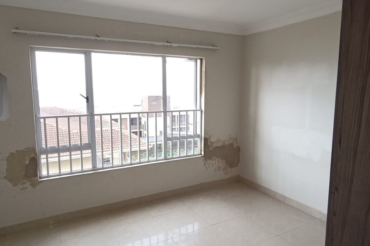 An empty bedroom featuring tiled flooring, a large window with security bars, and visible wall surface damage requiring repair.