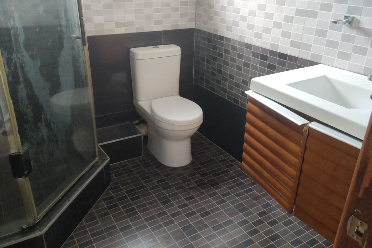 A compact bathroom featuring a glass-enclosed shower, a white toilet, and a wall-mounted vanity with a basin, finished with dark and patterned wall tiling.