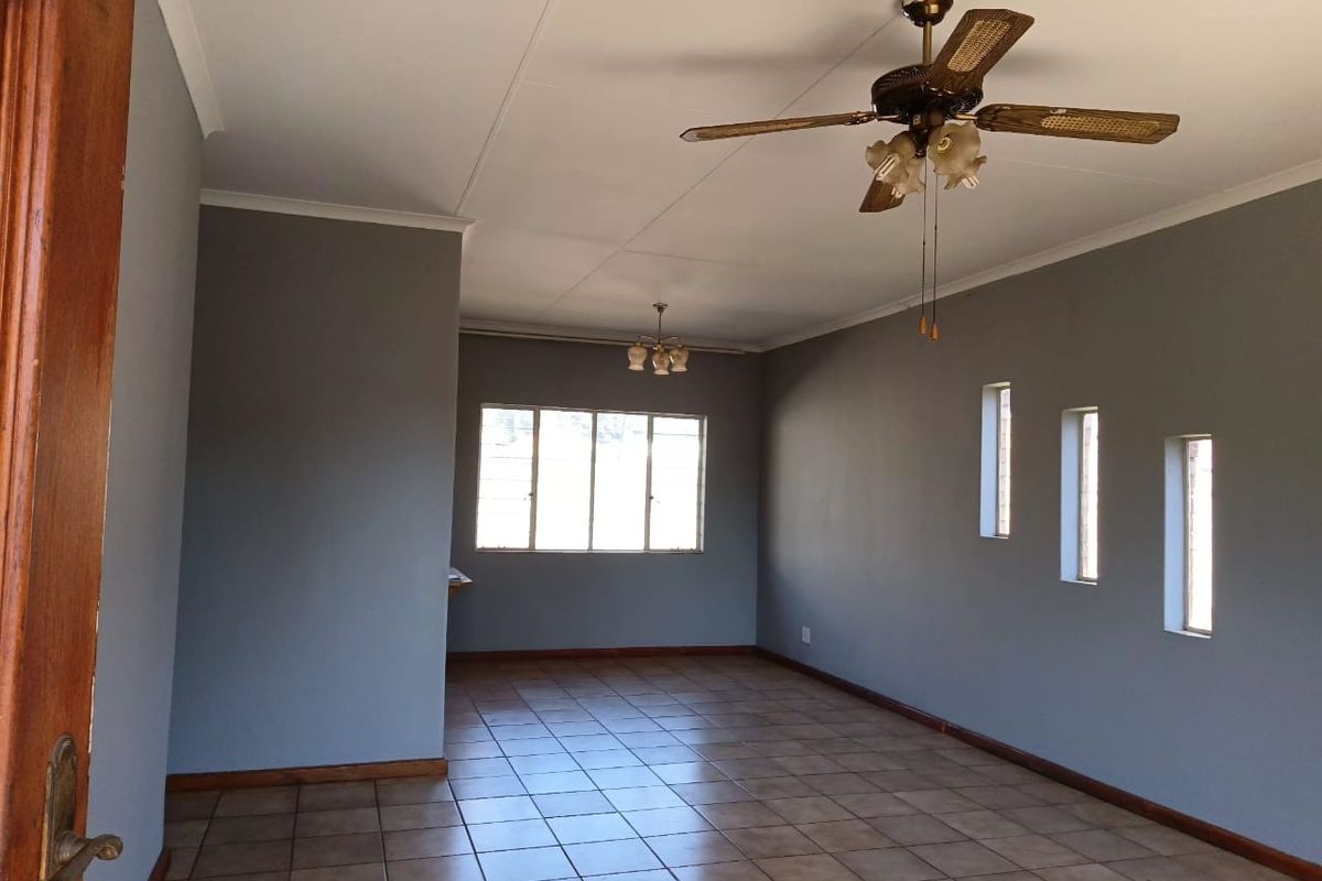 An empty living room featuring tiled flooring, neutral grey walls, ceiling fans, and multiple windows providing natural light.
