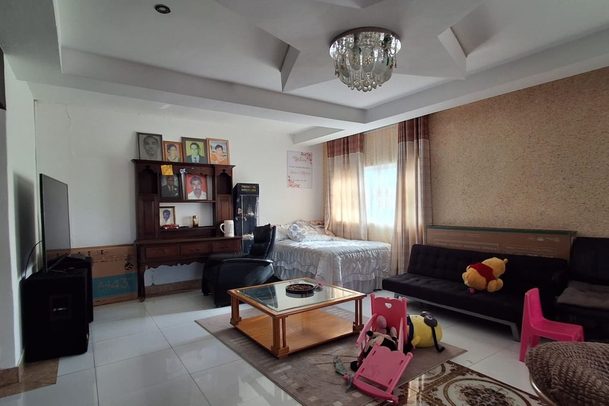 A spacious living area featuring a tray ceiling with a decorative chandelier, tiled flooring, and a textured accent wall.