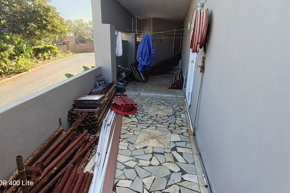 A narrow exterior side passage featuring stone-tiled flooring and a wall-mounted hose reel, currently used for storage.