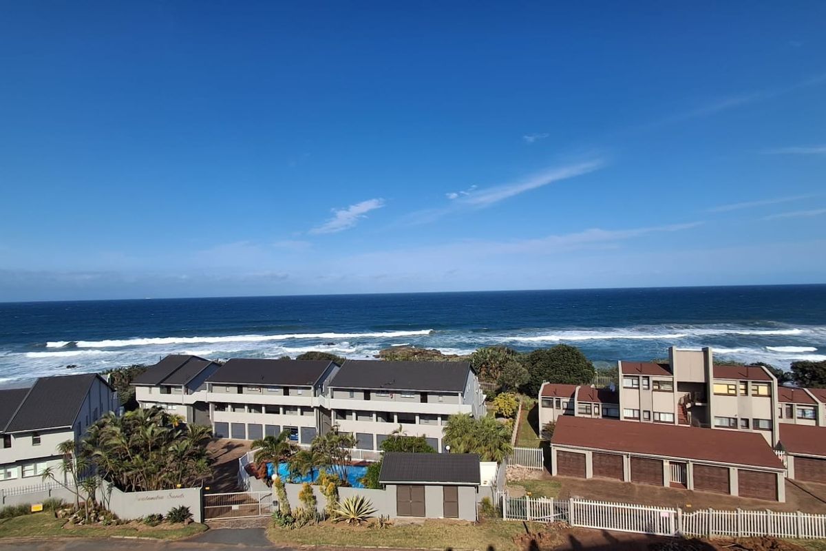 An elevated aerial view of a coastal commercial property complex featuring multiple buildings, a swimming pool, and direct ocean views.