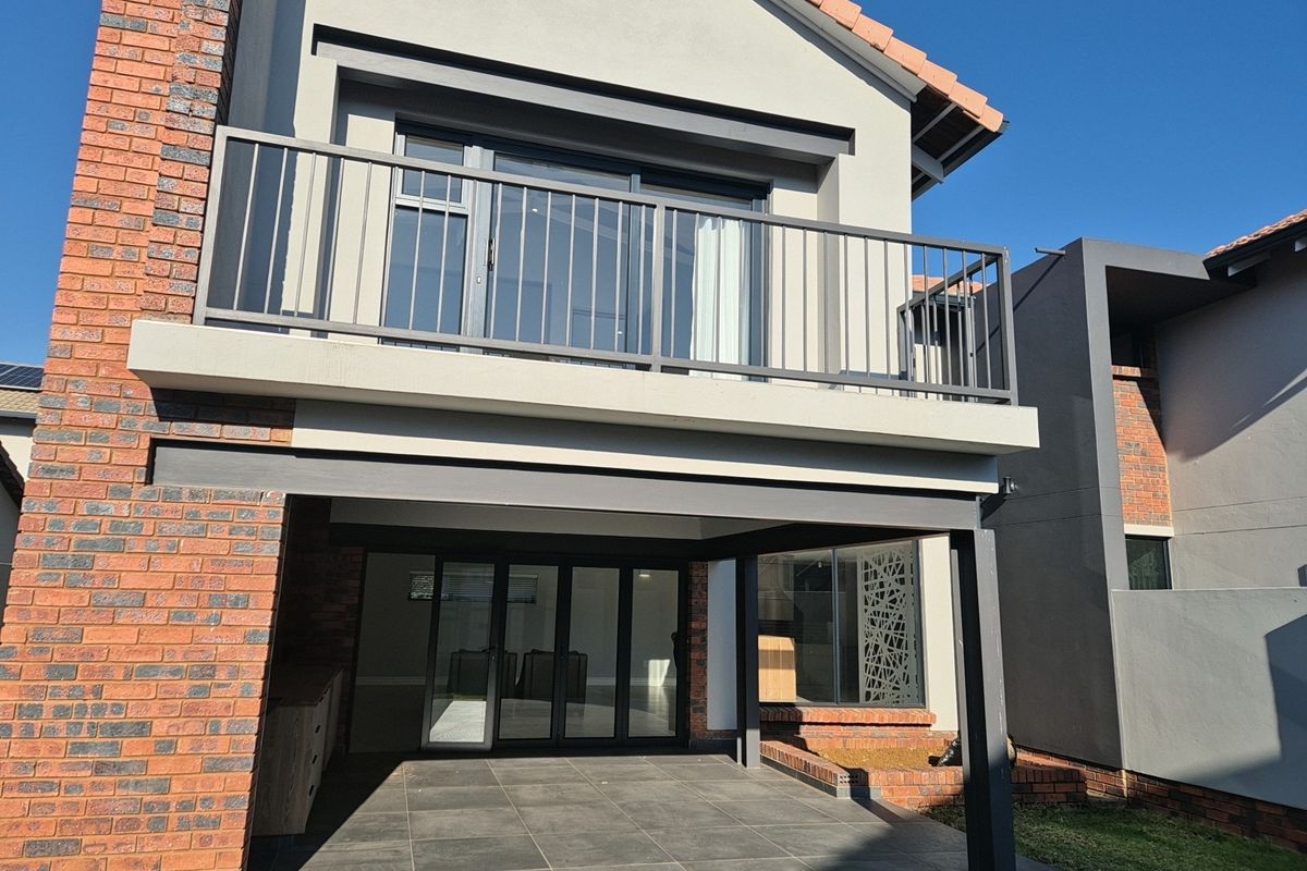Rear view of the property featuring a covered patio with tiled flooring and a balcony above with metal railings.