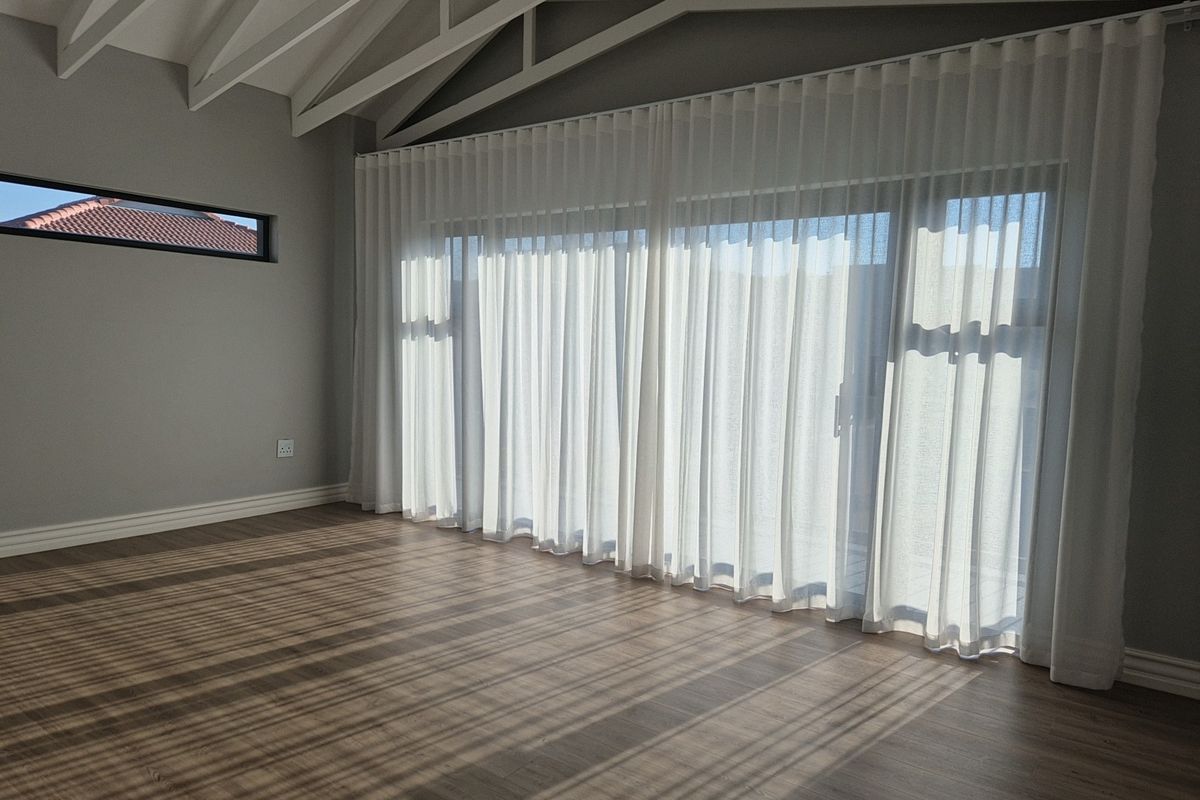 Bright and spacious living area featuring high vaulted ceilings, modern wood-look flooring, and large sliding glass doors with elegant sheer curtains.