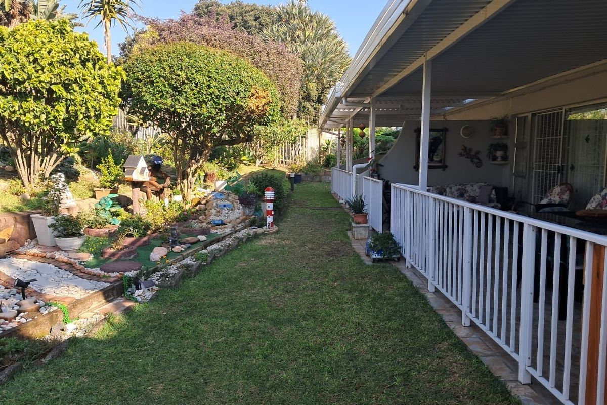 A well-maintained rear garden featuring a landscaped lawn, established trees, and a covered patio area with white balustrade railing.