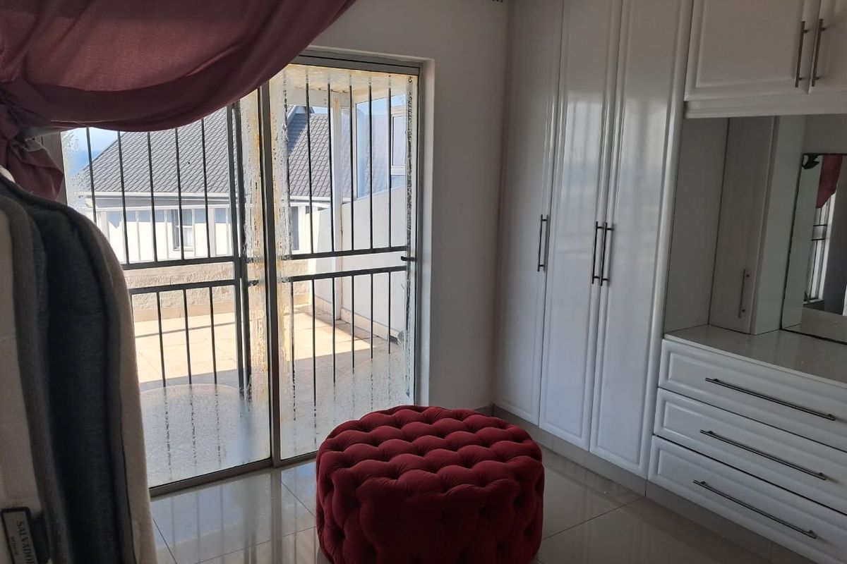 A bright bedroom featuring built-in white cabinetry, tiled flooring, and direct access to a private balcony through a secure sliding door.