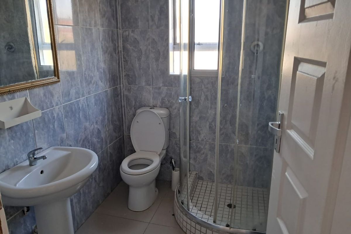 A functional bathroom featuring a pedestal basin, a close-coupled toilet, and a corner shower enclosure with tiled walls and flooring.