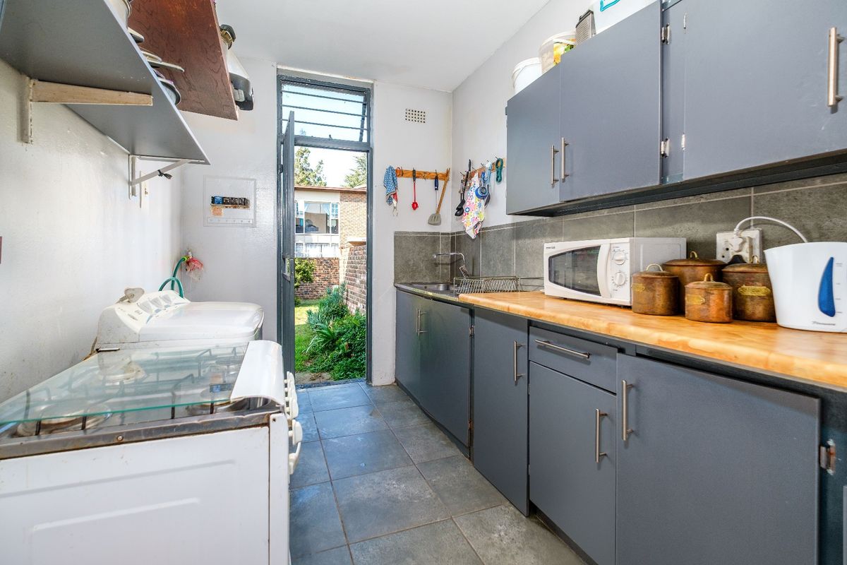 A functional galley-style kitchen featuring dark grey cabinetry, wooden countertops, tiled flooring, and direct access to the rear garden area.
