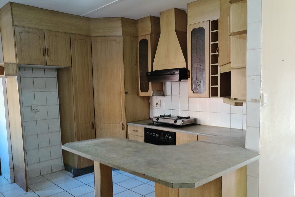 A dated kitchen featuring wooden cabinetry, a gas hob with extractor fan, tiled splashback, and a breakfast bar counter.