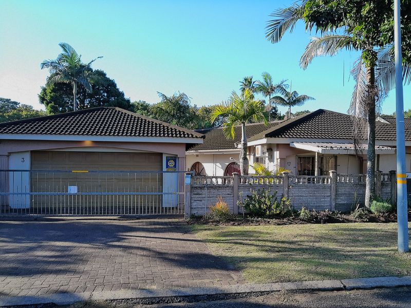Front elevation of a single-story house featuring a double garage, paved driveway, and perimeter wall with a sliding security gate.
