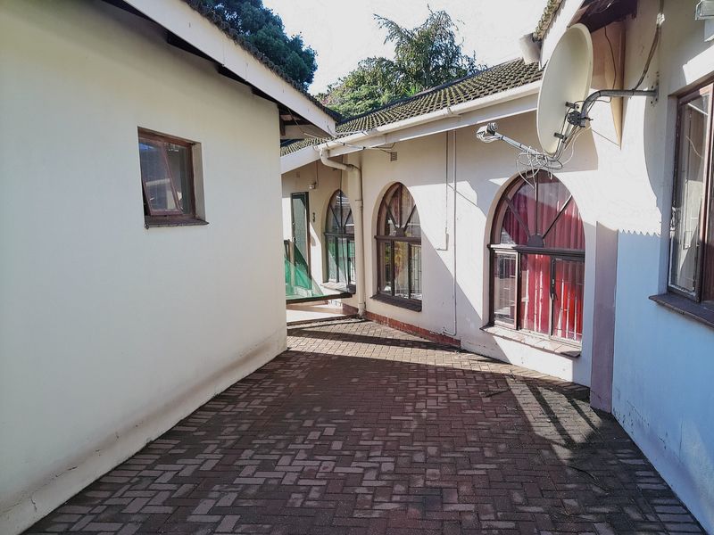A paved exterior walkway between building sections featuring arched windows, tiled roofing, and exterior wall finishes.