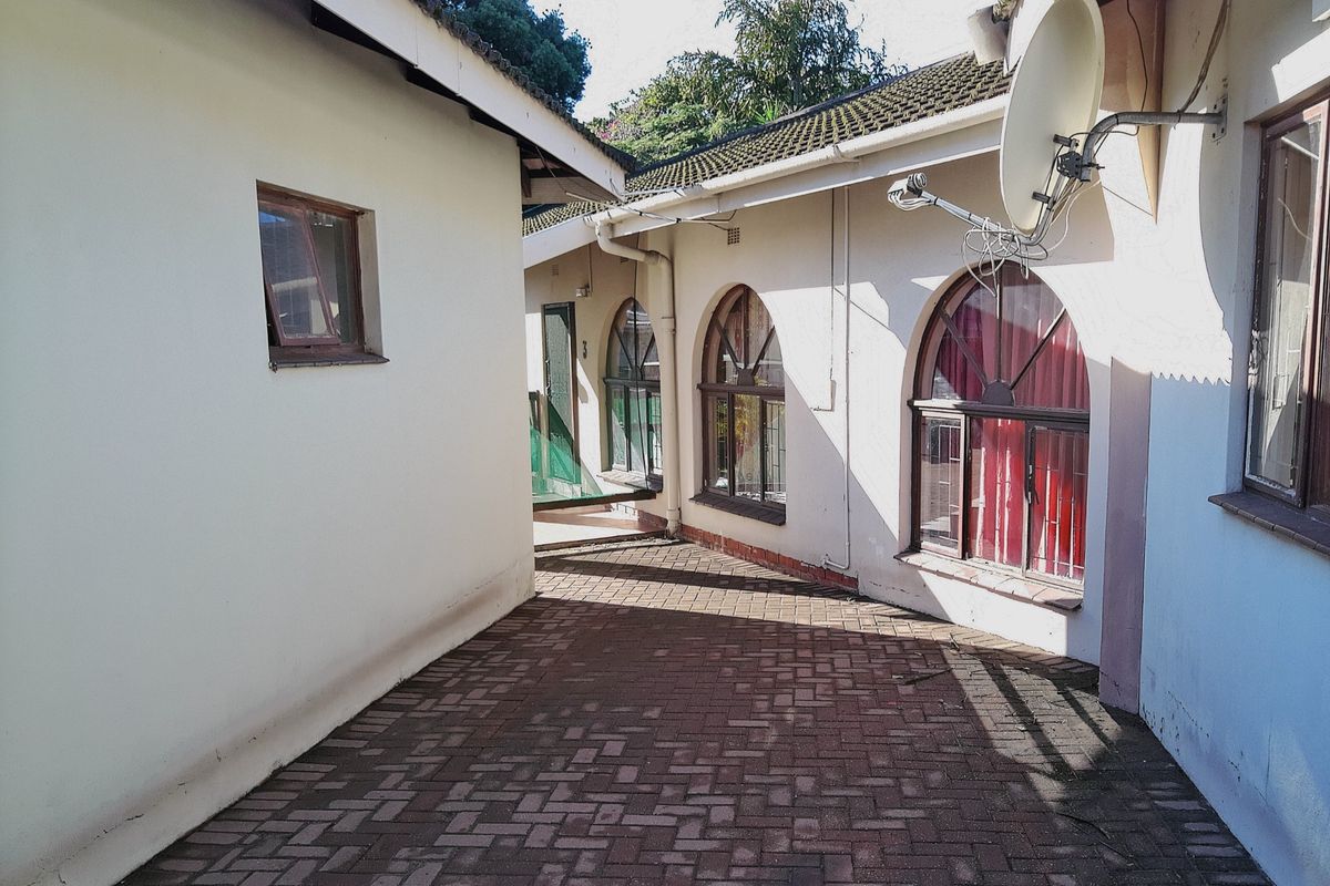 A paved exterior walkway between building sections featuring arched windows, tiled roofing, and exterior wall finishes.