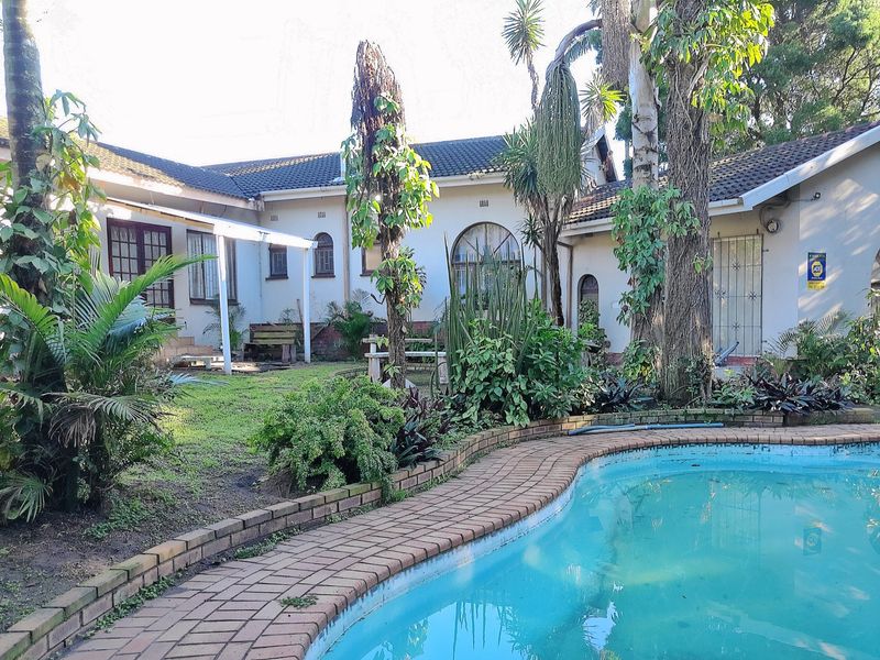 Rear garden area featuring a swimming pool with brick coping, surrounded by established trees and the rear elevation of the house.