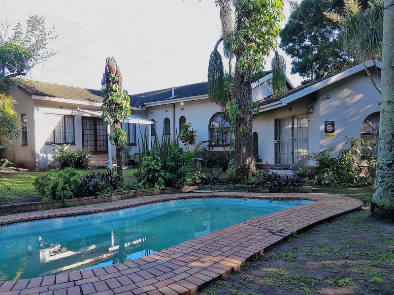 Rear view of the house featuring a swimming pool with brick coping, established garden, and security features on windows and doors.
