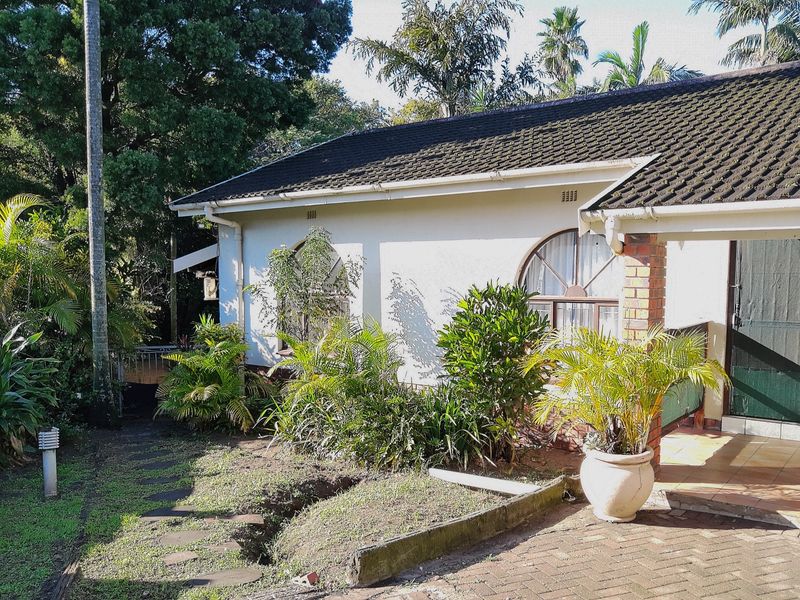 Front exterior view of a house featuring a tiled roof, arched windows, and a paved entrance area with established garden surroundings.