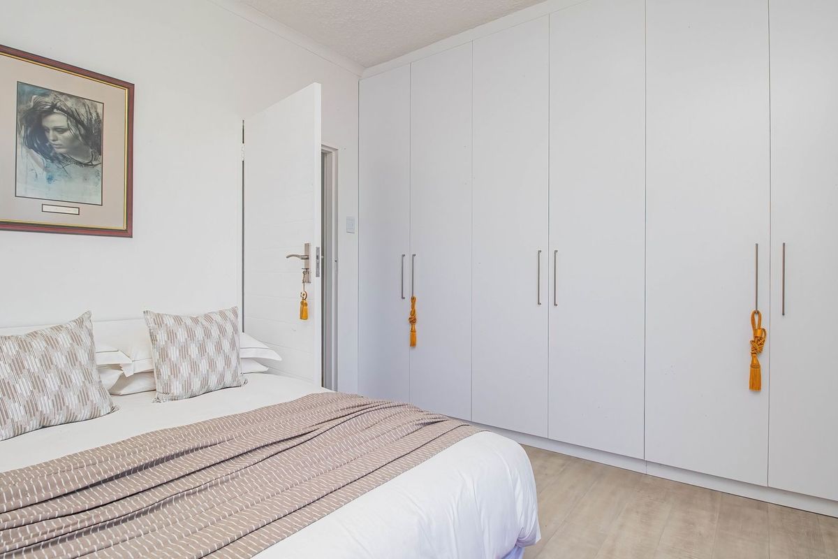 A well-maintained bedroom featuring extensive floor-to-ceiling built-in wardrobes with modern handles and light-toned laminate flooring.