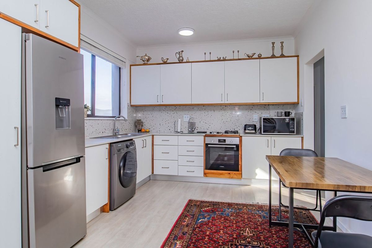 A functional kitchen featuring white cabinetry, speckled backsplash, integrated oven, and space for a washing machine, with an adjacent dining area.