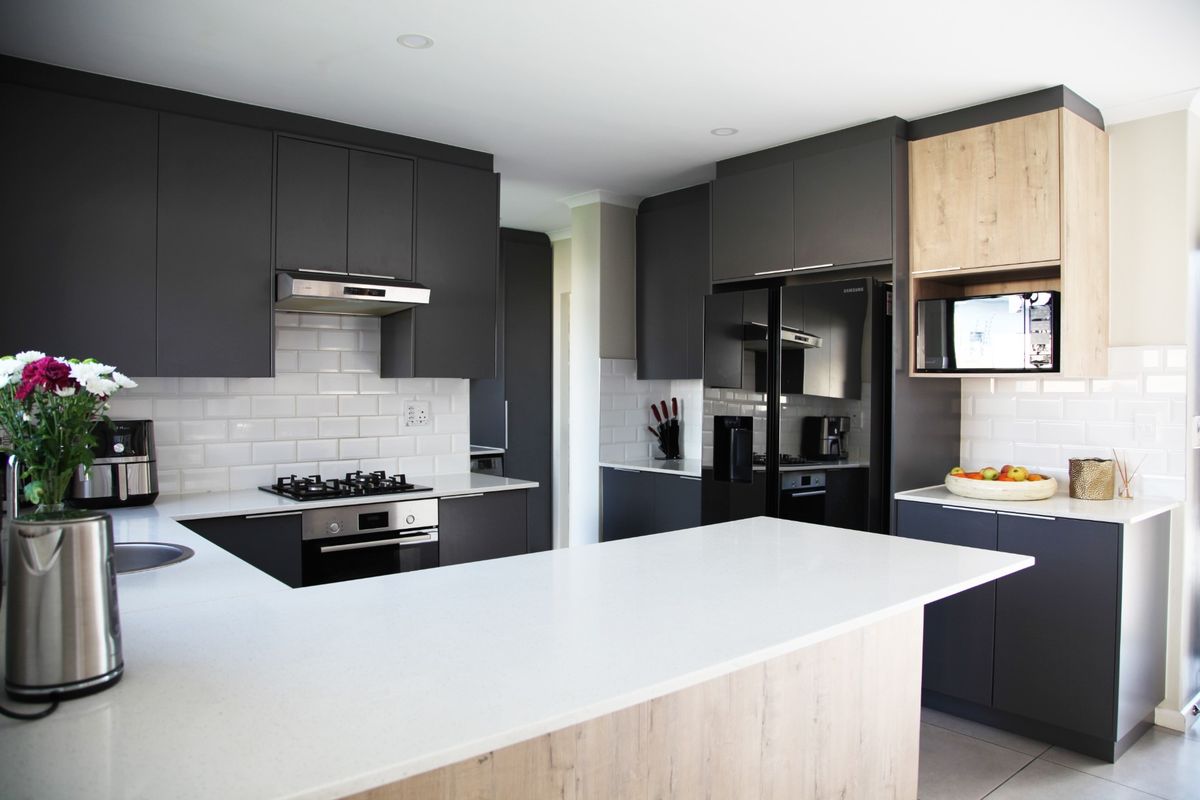 Modern kitchen featuring dark cabinetry, light wood accents, white stone countertops, subway tile backsplash, and integrated stainless steel appliances.