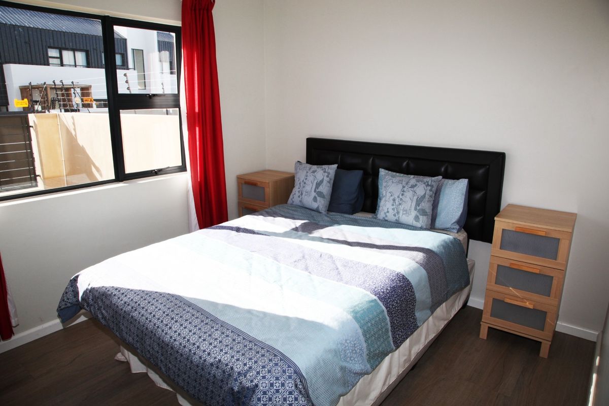 A well-lit bedroom featuring modern laminate flooring, a large window with black frames, and neutral wall finishes.