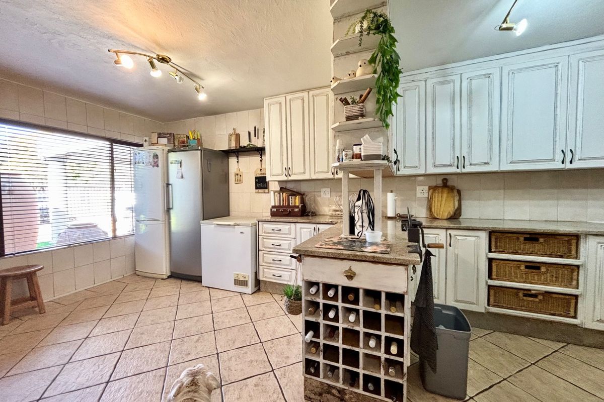 A rustic-style kitchen featuring white distressed cabinetry, granite countertops, a built-in wine rack, and tiled flooring with ample natural light.