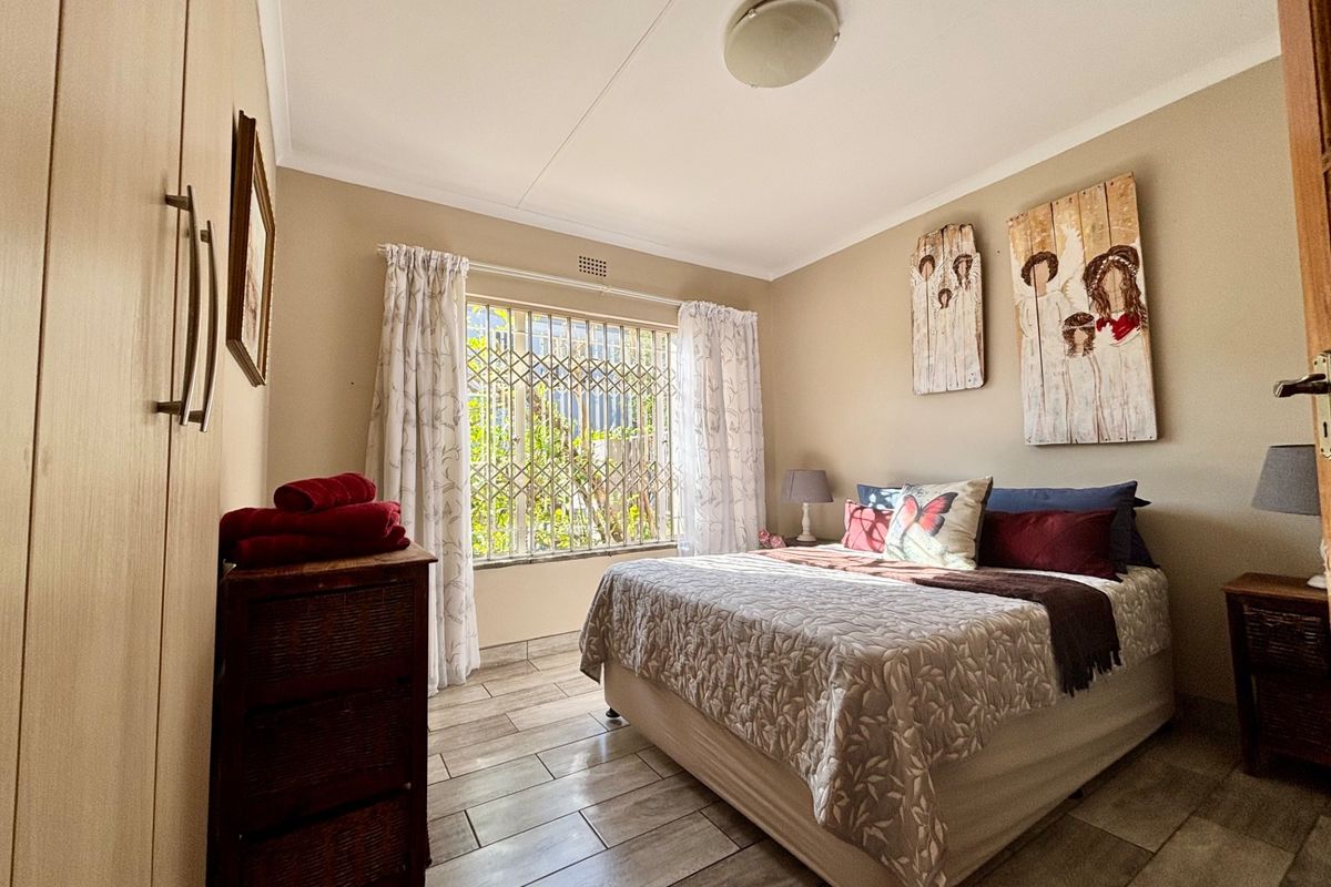 A well-maintained bedroom featuring tiled flooring, built-in wooden cupboards, and a window fitted with security bars.