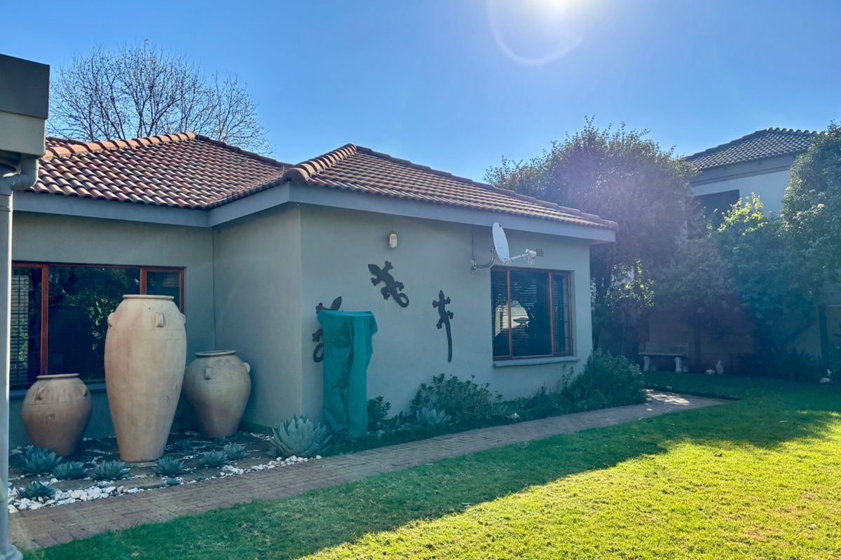 A view of the rear exterior of the house featuring a tiled roof, paved walkway, and landscaped garden area.