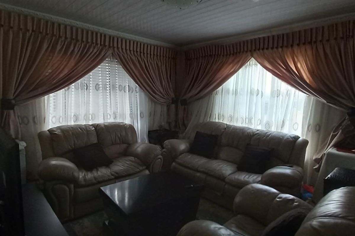 A living room featuring corner windows with draped curtains and a paneled ceiling.