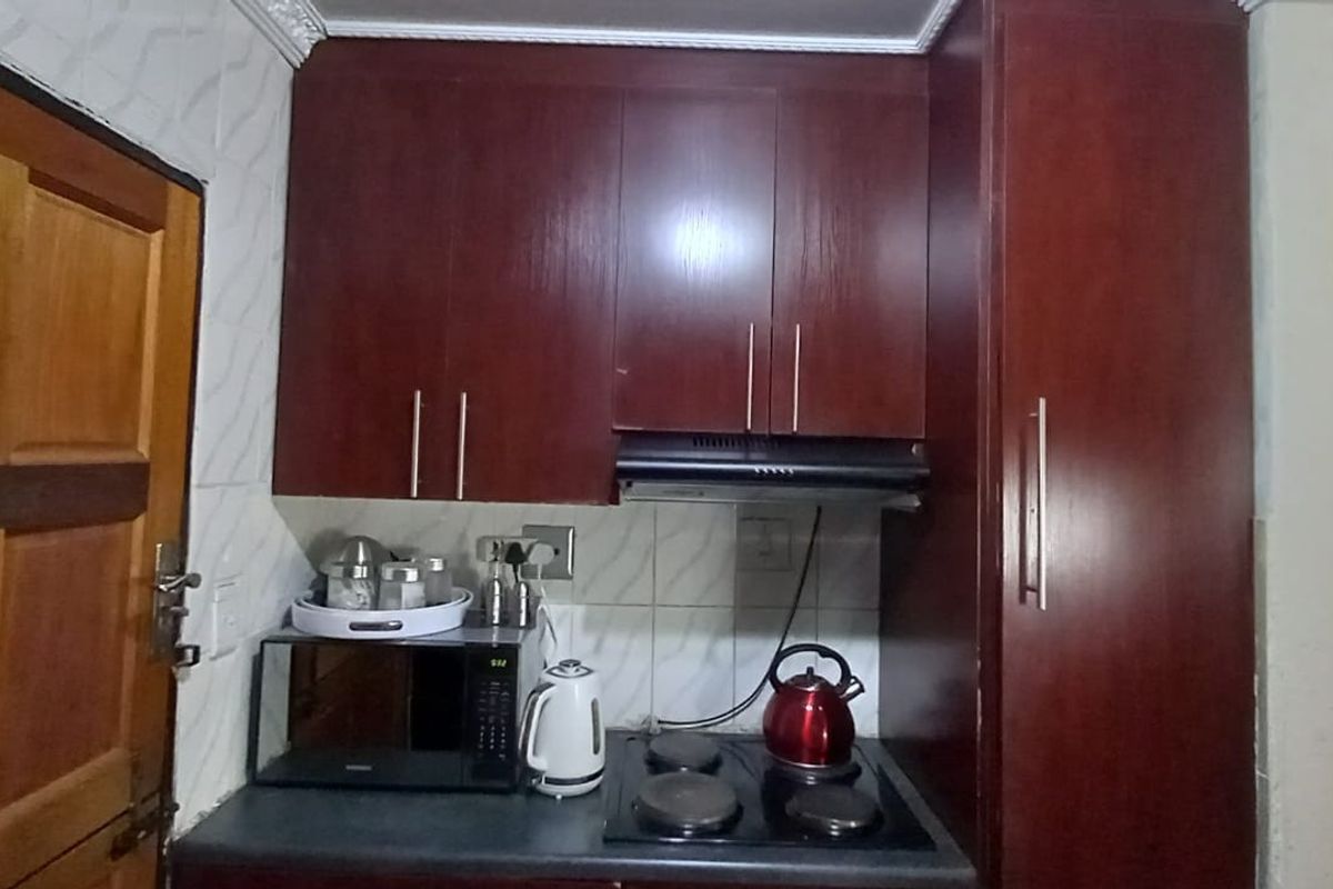 A compact kitchen area featuring dark wood-finish cabinetry, a built-in electric hob, and an integrated extractor fan.