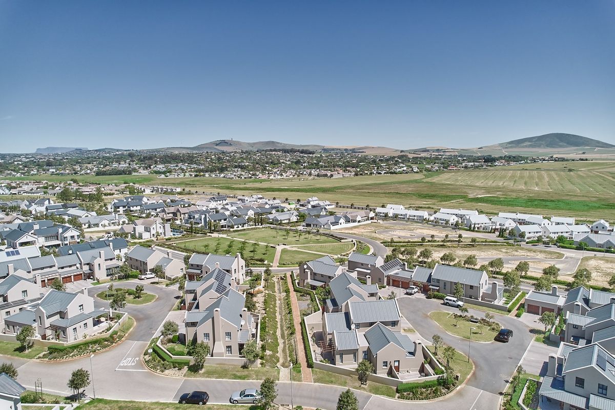 An aerial view of a modern residential estate featuring uniform housing, paved streets, and landscaped communal green spaces with mountain views.